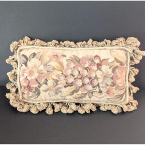 May include: A rectangular throw cushion featuring a woven floral tapestry pattern in shades of pink, cream, and muted green. The cushion is finished with a thick, twisted rope border and a dense fringe of small, knotted tassels along all four edges.