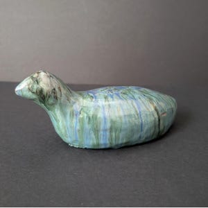 May include: A ceramic sculpture of a stylized bird in shades of blue, green, and white. The bird has a long, curved body and a small head with a pointed beak. The surface has a marbled effect.