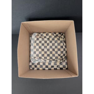 May include: A cardboard box with a black and white checkered pattern wrapping paper inside. The box is open, revealing the contents, which are partially visible. The background is a solid black surface.