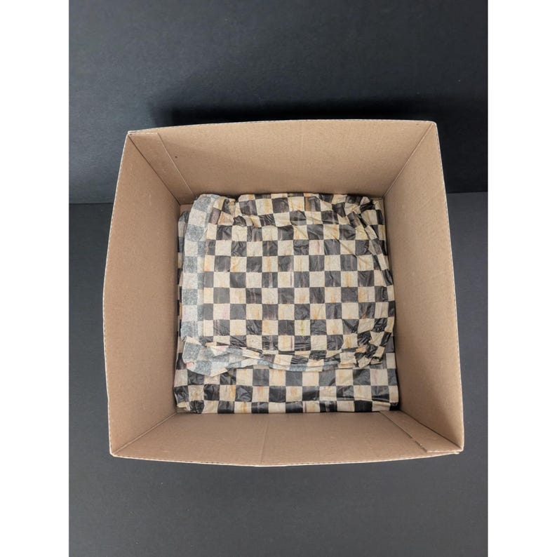 May include: A cardboard box with a black and white checkered pattern wrapping paper inside. The box is open, revealing the contents, which are partially visible. The background is a solid black surface.