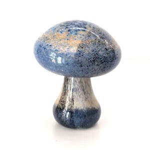 May include: A decorative glass mushroom sculpture. The mushroom cap is a speckled blue with hints of gold and brown. The stem is a gradient of silver and blue. The sculpture is set against a white background.