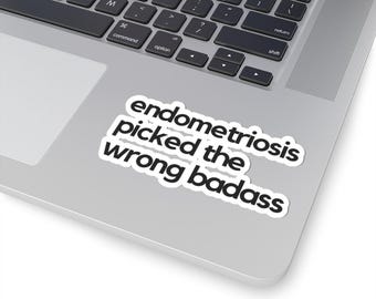 May include: A white sticker with black text that reads "endometriosis picked the wrong badass." The sticker is on a silver laptop.