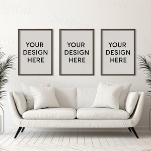 May include: Three brown picture frames with white mats hanging on a white wall above a white couch with white pillows. The frames have the text "YOUR DESIGN HERE" in black.