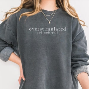 May include: A dark gray sweatshirt with the text "overstimulated and underpaid" printed in white on the front.