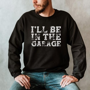 May include: A black sweatshirt with the text "I'll be in the garage" printed in white. The text is stylized with a tire tread pattern.
