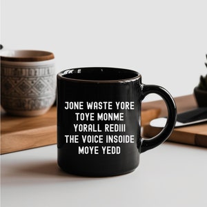 May include: Black ceramic coffee mug with white text that reads "Jone waste yore toye monme yorall rediii the voice insoide moye yedd".