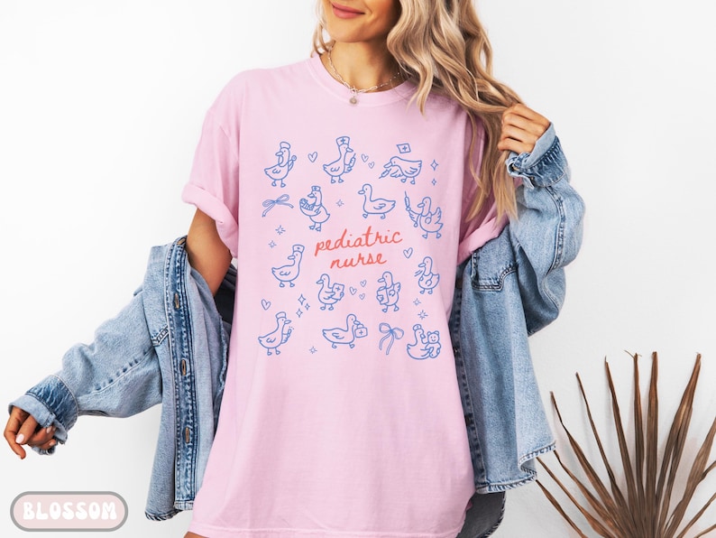 May include: Pink t-shirt with blue duck illustrations and the words "pediatric nurse" in red. The ducks are wearing nurse hats and holding medical supplies. A casual, comfortable tee.