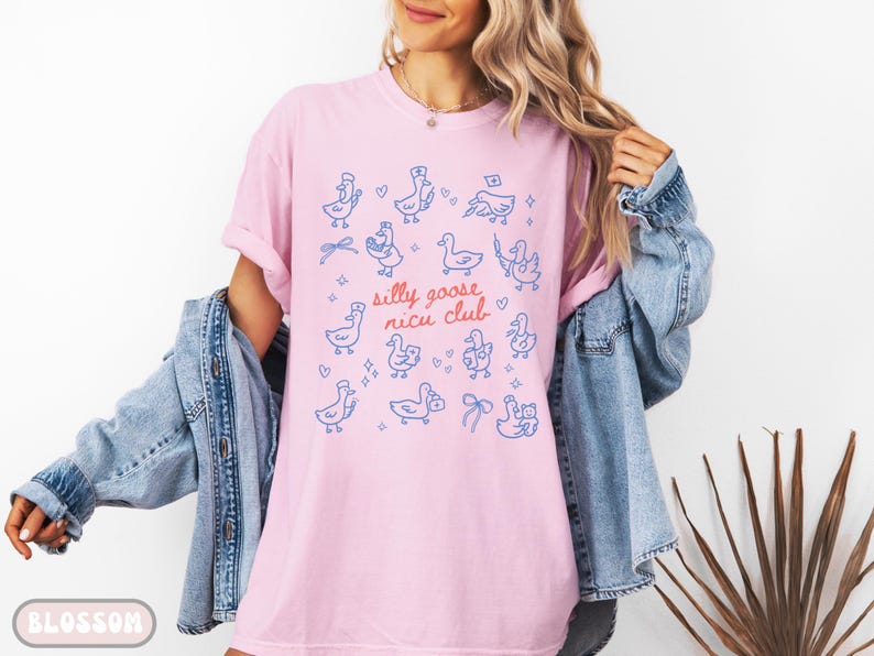 May include: A light pink t-shirt with a blue and red graphic of cartoon geese and the text "silly goose nicu club". The geese are in various poses, some wearing hats and bows. The shirt is made of soft material.