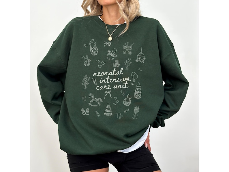 K&ouml;nnte beinhalten: Ein dunkelgr&uuml;ner Pullover mit einem wei&szlig;en Design aus babybezogenen Symbolen und dem Text "neonatal intensive care unit".