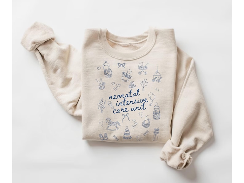 K&ouml;nnte beinhalten: Ein beiger Pullover mit einem blauen Design aus babybezogenen Symbolen und dem Text "neonatal intensive care unit".