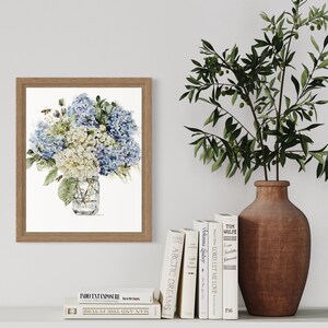 Pode incluir: Uma pintura em aquarela emoldurada de um buqu&ecirc; de hort&ecirc;nsias azuis e brancas em um frasco de vidro transparente. As flores est&atilde;o dispostas em um vaso com uma moldura de madeira marrom. A pintura est&aacute; em uma parede branca com uma oliveira em vaso e uma prateleira com livros.