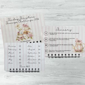 May include: A spiral-bound savings challenge calendar with a pink and white striped design. The cover reads "Sunday Scripture Savings Challenge 2026." Inside, the calendar features monthly savings goals and scripture verses, with a decorative teapot illustration.
