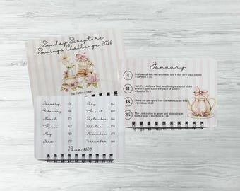 May include: A spiral-bound savings challenge calendar with a pink and white striped design. The cover reads "Sunday Scripture Savings Challenge 2026." Inside, the calendar features monthly savings goals and scripture verses, with a decorative teapot illustration.