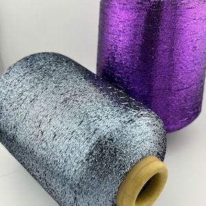 May include: Two spools of metallic thread, one silver and one purple. The spools are wound with thread and have wooden bobbins.
