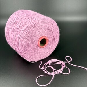 May include: A large spool of light purple yarn with a cardboard core. A length of the yarn is unwound and lies in a loose coil. The yarn is a soft, fuzzy texture, suitable for knitting or crocheting projects.