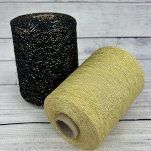 May include: Two spools of yarn, one black and one gold, with a glittery finish. The spools are sitting on a wooden surface.