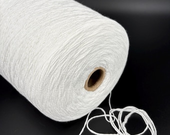 May include: A large spool of white yarn, ideal for knitting or crocheting projects. The yarn is tightly wound and has a textured appearance. A length of the yarn is unwound, showing its fine, individual strands. The background is a solid black.