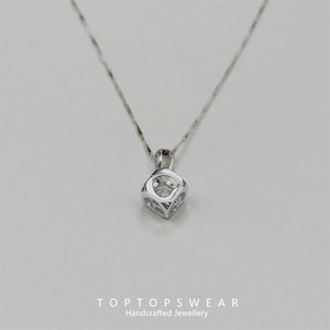 May include: A silver necklace with a square pendant featuring a clear, round gemstone. The pendant is encased in a geometric, open-work setting. The necklace is displayed on a white background. The text "TOPTOP SWEAR Handcrafted Jewellery" is at the bottom.