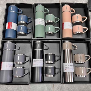 Puede incluir: Seis juegos de botellas de vacío aisladas de acero inoxidable con dos tazas a juego. Cada botella está etiquetada con "Botella de vacío 500 ml". Las botellas son de diferentes colores: gris, negro, verde, rosa y beige.