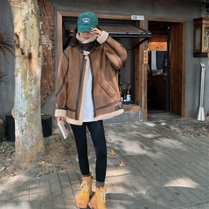 Op de afbeelding: Een bruin nep leren jack met een bontvoering en een ritssluiting. Het jack heeft een opstaande kraag en een klepzak op de linker borst. Het model draagt een zwarte legging en bruine laarzen.