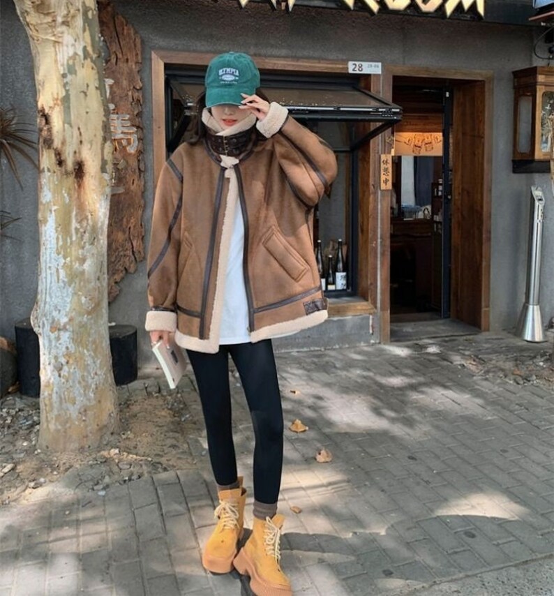Op de afbeelding: Een bruin nep leren jack met een bontvoering en een ritssluiting. Het jack heeft een opstaande kraag en een klepzak op de linker borst. Het model draagt een zwarte legging en bruine laarzen.
