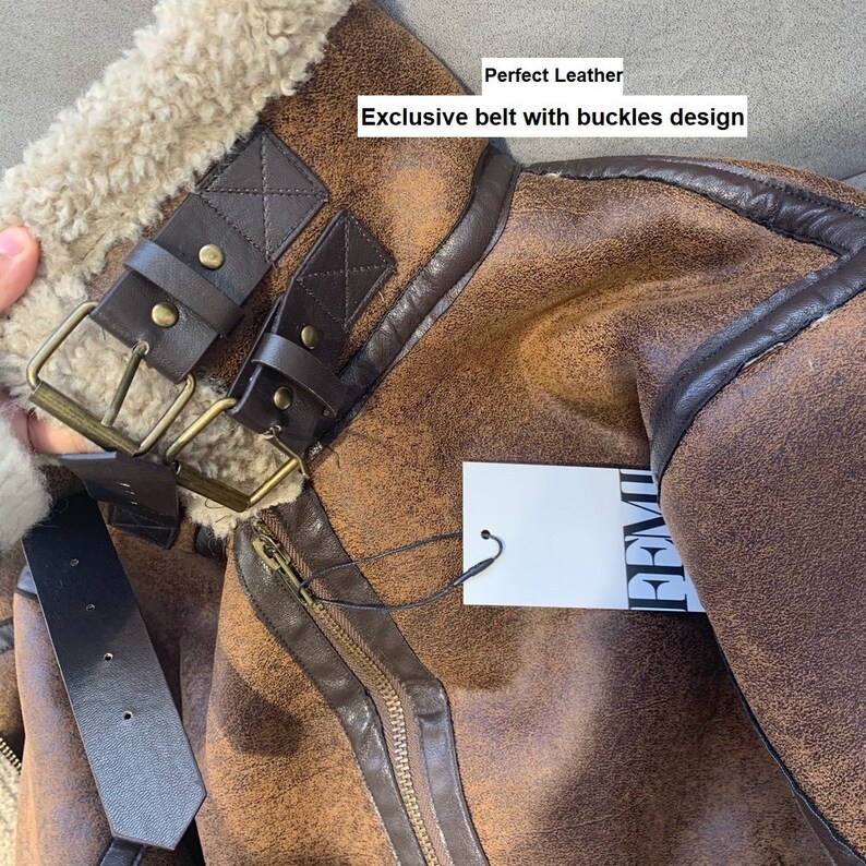 Op de afbeelding: Close-up van een bruin leren jack met een bontkraag en een bruine leren riem met gespen. Het jack heeft een ritssluiting en een label met de tekst "PREMIUM". De tekst "Perfect Leather" en "Exclusive belt with buckles design" is zichtbaar op de afbeelding.