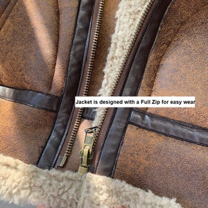 Op de afbeelding: Close-up van een bruin nep leren jack met een bruine rits en een bruine nep bont voering. De tekst "Jacket is designed with a Full Zip for easy wear" is zichtbaar op de afbeelding.