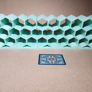 May include: A light blue honeycomb-shaped shelf unit with 24 compartments. The shelf unit is made of plastic and is sitting on a brown surface. A blue card with a gold design is in front of the shelf unit.