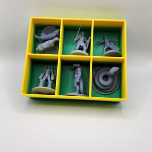 May include: A set of six miniature figurines in a green and yellow plastic storage box. The figurines are gray and include a snake, a warrior, a creature with wings, and three other figures.