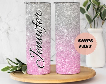 May include: Two personalized stainless steel tumblers with a pink and silver glitter ombre design. The tumbler on the left has the name "Jennifer" printed on it.