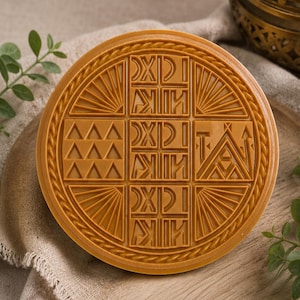Könnte beinhalten: Eine runde, bernsteinfarbene Form mit einem zentralen Gitter aus geometrischen Symbolen und Buchstaben. Das Design umfasst wiederkehrende Muster aus Dreiecken, vertikalen Linien und stilisierten Zeichen innerhalb eines kreisförmigen Rahmens.