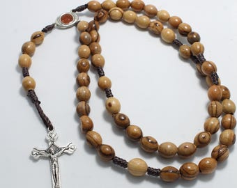 Può includere: Un rosario di legno marrone con un crocifisso d'argento e una piccola perla di pietra rossa. Il rosario è infilato su un cordoncino marrone.