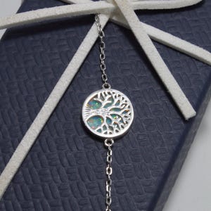 May include: A silver chain bracelet with a round pendant featuring a tree of life design with an iridescent opal stone in the center.