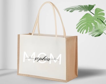 Könnte beinhalten: Eine beige Tragetasche mit einem weißen Feld, auf dem der Text "MOM sophia" in Schwarz und Weiß steht. Die Tasche hat einen braunen Jutegriff.
