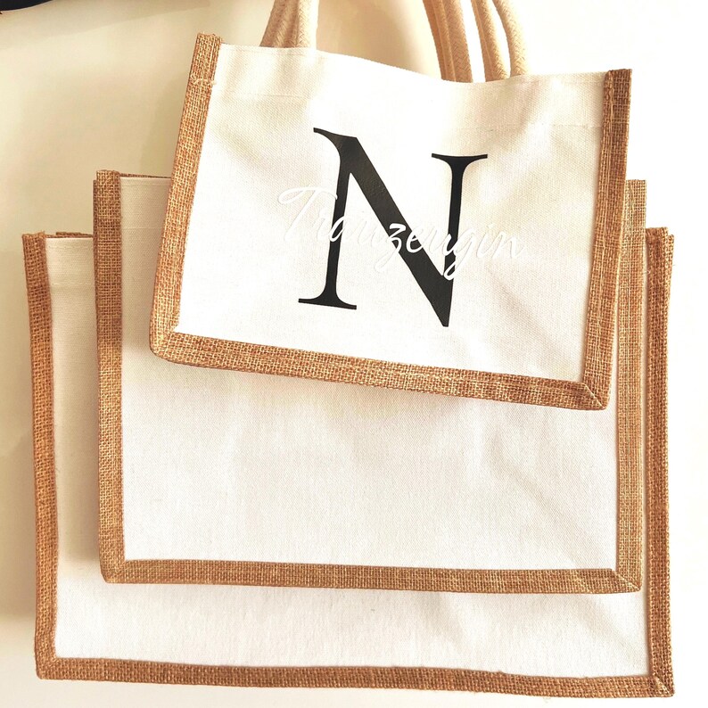 May include: Three white canvas tote bags with brown hessian trim. The largest bag has a black letter "N" printed on the front.