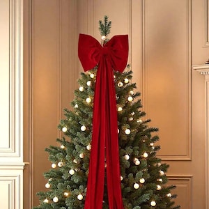 May include: A Christmas tree decorated with white lights and gold baubles, topped with a large red velvet bow and matching draped fabric. The tree is a festive centrepiece, perfect for the holiday season.
