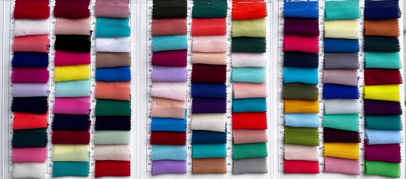 May include: A comprehensive fabric colour swatch chart featuring a grid of numerous small, rectangular textile samples in a wide variety of solid colours, including shades of red, blue, green, yellow, pink, purple, black, white, and neutral tones.