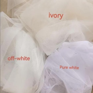 May include: Three swatches of sheer, fine-mesh tulle fabric arranged in overlapping layers. The fabric colors are labeled with text as ivory, off-white, and pure white, showcasing the distinct tonal differences between these three shades of white.