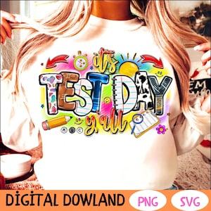 Könnte beinhalten: Ein weißes T-Shirt mit einem bunten Grafikdesign, auf dem "It's Test Day Y'all" steht. Das Design enthält verschiedene schulbezogene Elemente wie einen Bleistift, ein Lineal, ein Buch und eine Uhr.