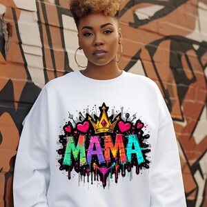 May include: White sweatshirt with a colorful graphic print of the word "MAMA" with a crown and hearts. The graphic has a graffiti style with dripping paint.
