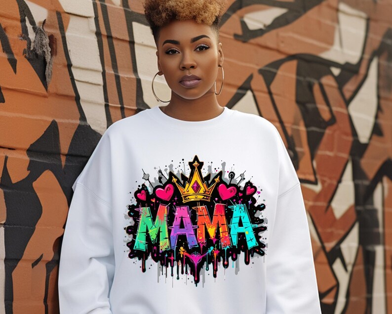 May include: White sweatshirt with a colorful graphic print of the word "MAMA" with a crown and hearts. The graphic has a graffiti style with dripping paint.