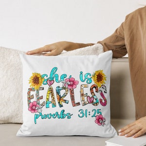 May include: White square pillow with the text "she is FEARLESS proverbs 31:25" in a colorful, floral design. The pillow features sunflowers, pink flowers, and a heart. The pillow is on a white couch.