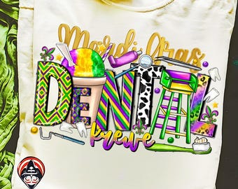 May include: Cream-colored t-shirt with a colorful graphic design. The design features the words "Mardi Gras Dental Krewe" with dental-themed imagery, including a snow cone, dental tools, and a toothbrush. The letters are decorated with purple, green, and gold patterns.