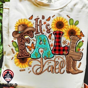 May include: Cream-colored t-shirt with a colorful graphic that reads "It's Fall Y'all." The design incorporates a cowboy hat, sunflowers, cacti, butterflies, and cowboy boots. The letter "L" is in a red and black plaid pattern.