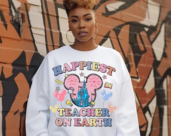 May include: White sweatshirt with the text "Happiest Teacher on Earth" in colorful letters. The design includes a Mickey Mouse head with a castle, balloons, and school-themed icons. The sweatshirt is a crew neck style.