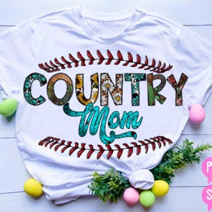 Könnte beinhalten: Weißes T-Shirt mit einem Baseball-Nahtdesign und dem Text "Country Mom" in Blumenbuchstaben.