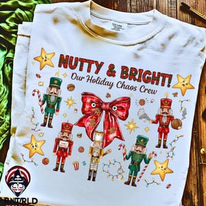 Może przedstawiać: Biała koszulka z świątecznym wzorem z napisem "Nutty & Bright! Our Holiday Chaos Crew". Koszulka prezentuje kolorowe ilustracje dziadków do orzechów, gwiazd i dużej kraciastej kokardy, idealnej na sezon świąteczny.