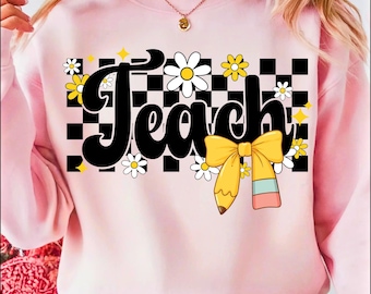 May include: A light pink sweatshirt with the word "Teach" in large black letters. The word is set against a black and white checkered background, with daisies and a yellow pencil with a bow. The sweatshirt is a crew neck style.