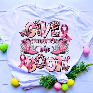 Könnte beinhalten: Weißes T-Shirt mit einem rosa Band, rosa Cowboystiefeln und dem Text "Give cancer the boot".
