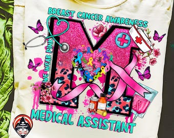 May include: Cream-colored t-shirt with a pink glitter "M" design for Breast Cancer Awareness. The design includes a stethoscope, ribbons, butterflies, and the words "We Wear Pink" and "Medical Assistant."
